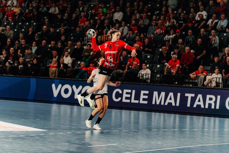 Jucătoare Gloria Bistriţa în acțiune ofensivă în meciul din handbal feminin Liga Națională, cu tabela clasament handbal feminin în fundal. | sursa foto: News.ro Jucătoare Gloria Bistriţa în acțiune ofensivă în meciul din handbal feminin Liga Națională, cu tabela clasament handbal feminin în fundal. | sursa foto: News.ro
