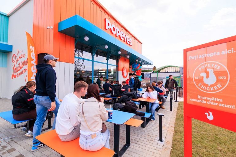 Logo Rex Concepts pe fațada unui restaurant modern, cu angajați în uniformă pregătind deschiderea noii locații în cadrul extinderii restaurante din România, evidențiind creșterea veniturilor Rex Concepts franciză. | sursa foto: Profit